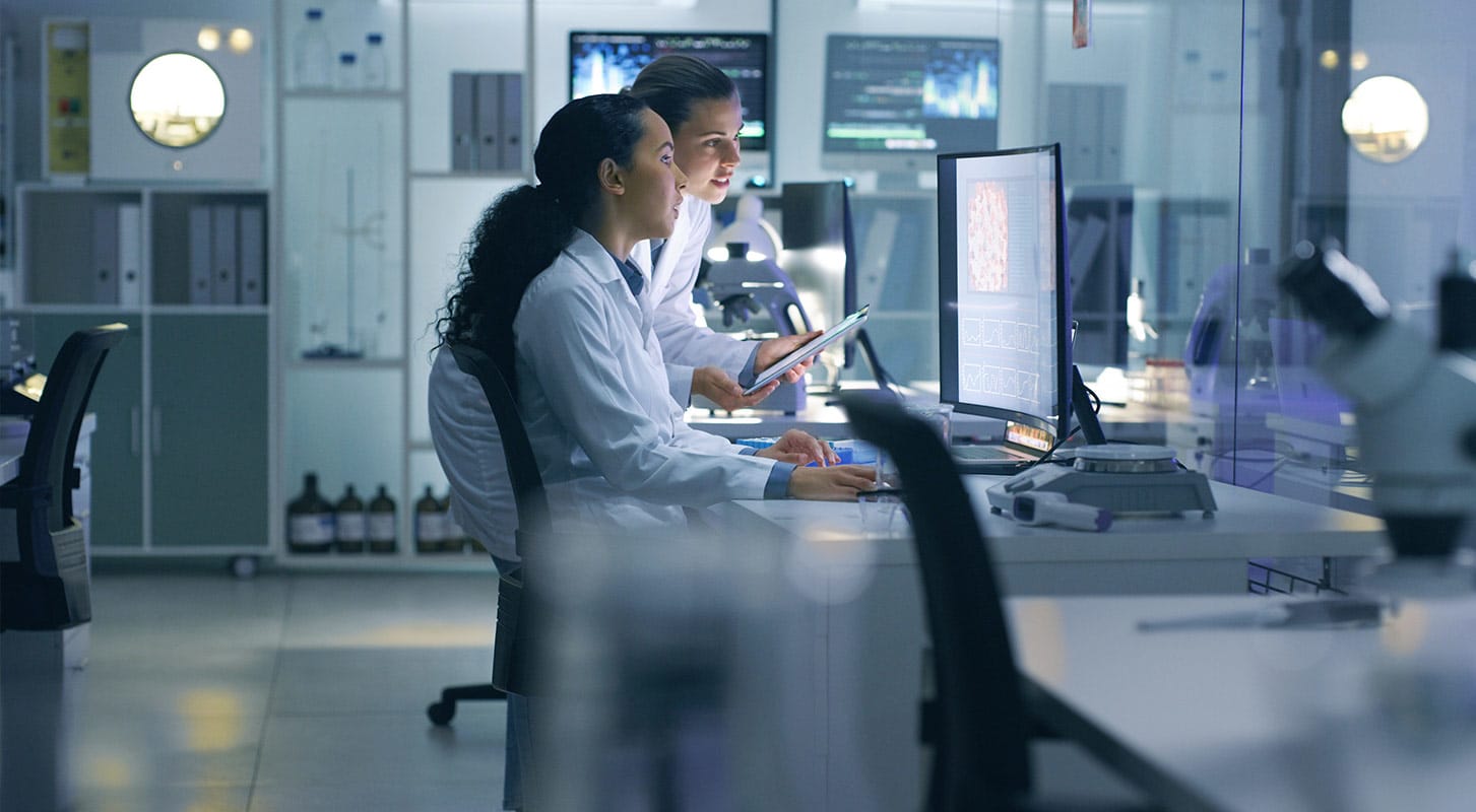 Two medical personnel in lab coats analyzing data on computers.